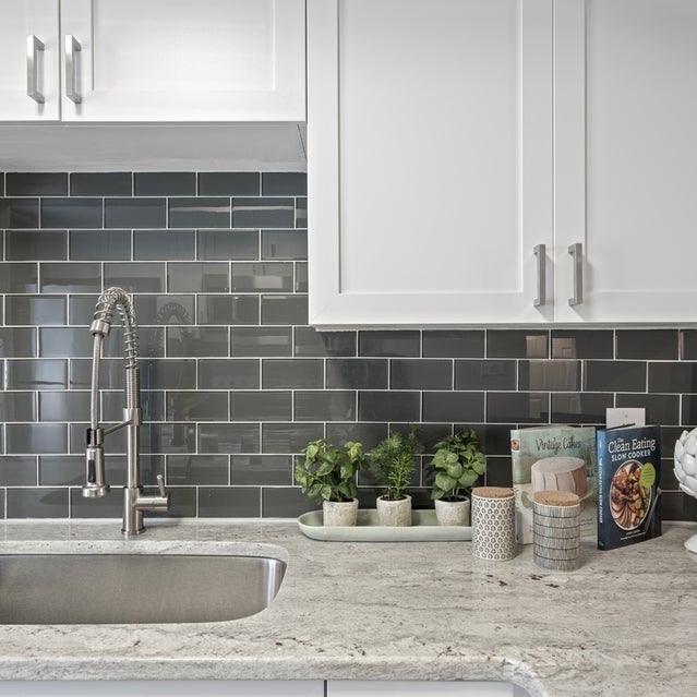 Andover At Crabtree Apartments - Kitchen With Farmhouse Sink, White Cabinetry, And Dark Gray Subway Tile Backsplash