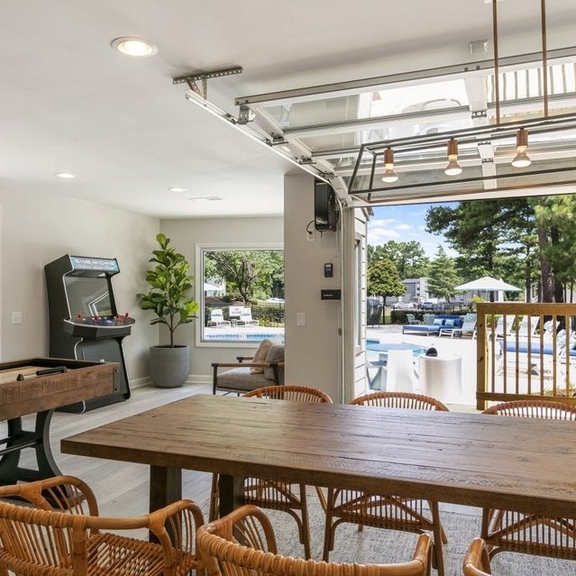 Andover at Crabtree Apartments - clubhouse with dining table and games overlooking pool